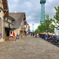 people are walking down the sidewalk in front of some buildings with a tower in the background