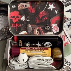 an open tin with various items in it on top of a table next to stickers