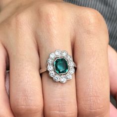 a woman's engagement ring with an emerald and diamond center surrounded by white diamonds