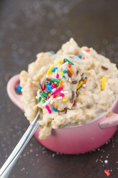 a pink bowl filled with oatmeal and sprinkles next to a spoon