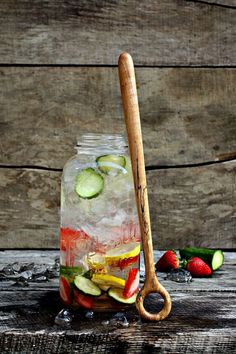 a jar filled with ice, cucumber and strawberries next to a wooden spoon