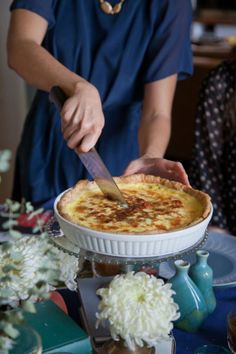 a person cutting into a pie on top of a blue table cloth with flowers in the background