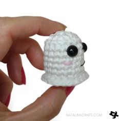 a hand holding a tiny white crocheted sheep ornament with black eyes