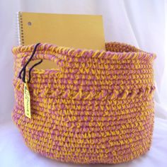 a pink and yellow crocheted basket with a notepad in the bottom corner