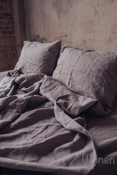 an unmade bed with two pillows on top of it and a brick wall in the background