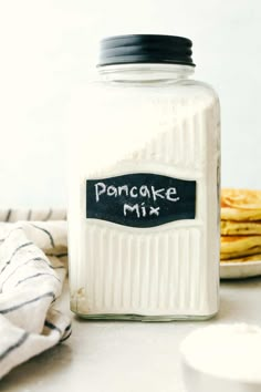 a glass jar filled with pancake mix on top of a table next to pancakes