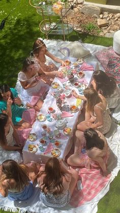 a group of women sitting at a picnic table eating cake and drinking tea outside in the sun