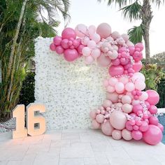 a large balloon arch with pink and white balloons in front of the number sixteen sign