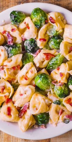 a white plate topped with pasta and broccoli covered in cheese sauce on top of a wooden table