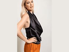 a woman with blonde hair wearing an orange pants and black top standing in front of a white wall