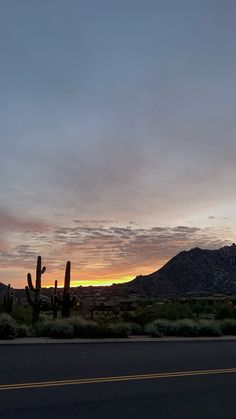 the sun is setting in the desert with cactus and mountains in the backgroud