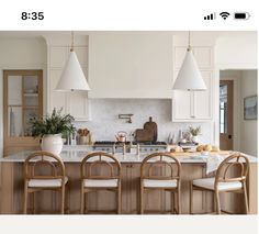 an image of a kitchen setting with white cabinets and wooden chairs in the center island