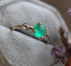 a ring with an oval green stone surrounded by small white diamonds sits on a cushion