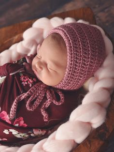 a newborn baby wearing a pink bonnet and sleeping in a wooden bowl on a table