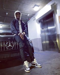 a man sitting on top of a car in front of an open door and wearing sneakers