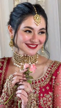 a woman in a red and gold bridal outfit holding a rose with her hands