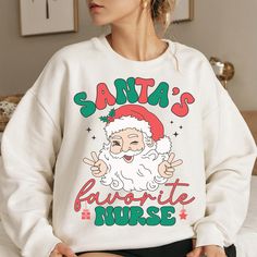 a woman sitting on top of a bed wearing a santa's favorite nurse sweatshirt