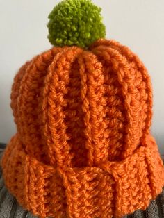 an orange crocheted hat with a green pom - pom on top