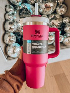 a person holding a pink travel mug in front of a christmas ornament display