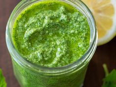 a green smoothie in a mason jar next to sliced lemons and parsley