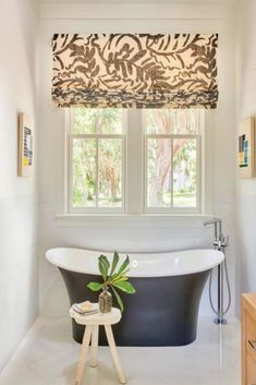 a bath tub sitting under a window next to a wooden table with a potted plant on it