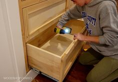 a young boy kneeling down to look at something in a wooden drawer with a light on it