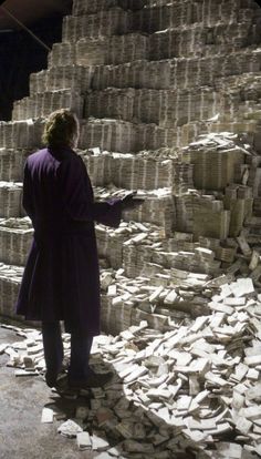 a man in a purple coat standing next to stacks of cement bricks and looking at something on the ground