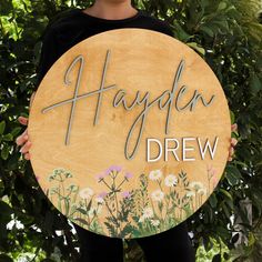 a person holding up a wooden sign that says,'happily drew'in front of some trees