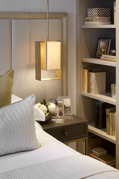 a bed with white sheets and pillows in a bedroom next to a bookshelf