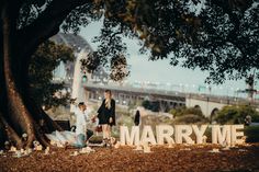 two people standing next to each other in front of a sign that says marry me