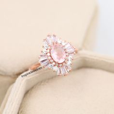 a pink diamond ring sitting on top of a cushion