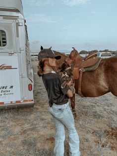 a woman standing in front of a horse next to a trailer with a brown horse