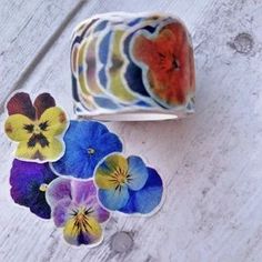 several pansies are sitting on a white surface next to a paper plate with flowers painted on it