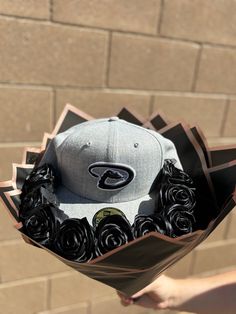 a hat with roses in it is held up by someone's hand against a brick wall