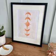 a wooden table topped with a white vase filled with flowers and a framed art piece