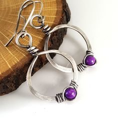 Eco friendly sterling silver (16G) has been hand formed and hammered into hoops. An organic spiral has been wire wrapped around a 4mm purple fossil stone bead. The hoops have been oxidized and lightly brushed with steel wool and then polished for a soft patina. Perfect earrings for the holidays! Ear wires are hand formed from sterling silver. Earrings measure 1.75 inches from top of ear wire to bottom of teardrop. The widthr at widest part is 7/8 of an inch. All silver used has come from a recyc Purple Metal Drop Earrings, Handmade Purple Metal Earrings, Purple Metal Earrings As Gift, Purple Metal Earrings For Gift, Purple Round Metal Earrings, Adjustable Metal Teardrop Earrings For Gift, Adjustable Metal Teardrop Earrings Gift, Purple Teardrop Metal Earrings, Purple Teardrop Metal Jewelry