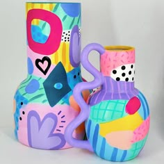 two colorful vases sitting next to each other on a white surface with hearts and shapes painted on them