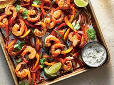 a tray filled with shrimp, peppers and limes next to a bowl of sour cream