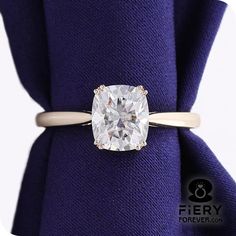 a cushion cut diamond ring on top of a purple napkin