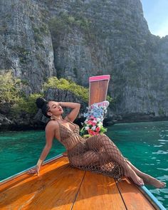 a woman laying on top of a wooden boat in the ocean next to some cliffs