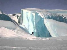 a man standing on top of a snow covered slope next to an iceberg in the middle of nowhere