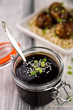 a jar filled with black sauce and topped with green onions next to another container full of meatballs