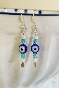 This pair of silver plated earrings features silver plated ear wires, hoops and paddle pins, along with light teal and white czech glass beads and classic evil eye protection 🧿 beads. Each pair of earrings comes with silicone stoppers to hold the earring in place securely. These measure 1.75 inches in total length. o ~ TURNAROUND TIME ~ Ready to ship items, such as earrings, will ship in 1-2 business days.  o ~ CUSTOMER CARE ~ Please contact us if you have any questions or need help placing an Diy Earrings Dangle, Bohemian Jewels, Earrings Diy Handmade, Protection Jewelry, Evil Eye Protection, Beaded Earrings Diy, Easy Jewelry, Diy Jewelry Unique, Beads For Sale