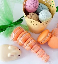 an assortment of macaroons in a basket next to a fake bunny and carrot