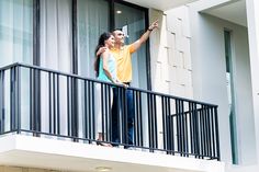 a man and woman standing on a balcony pointing at the sky with their arms in the air