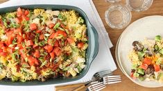 two plates with pasta and vegetables on them next to silverware, glasses and utensils