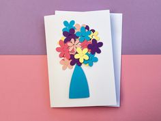 a card with flowers in a blue vase on a pink and purple tablecloth background