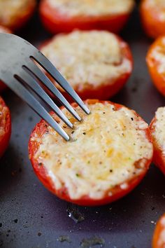 a fork is stuck into some tomatoes with cheese on them and other toppings are in the background