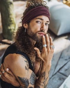 a man with long hair wearing a bandana and holding his hand to his face