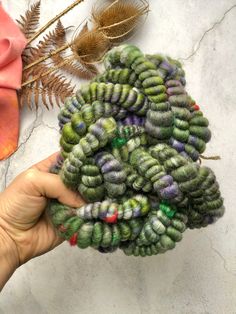 a hand holding a bunch of green and purple flowers